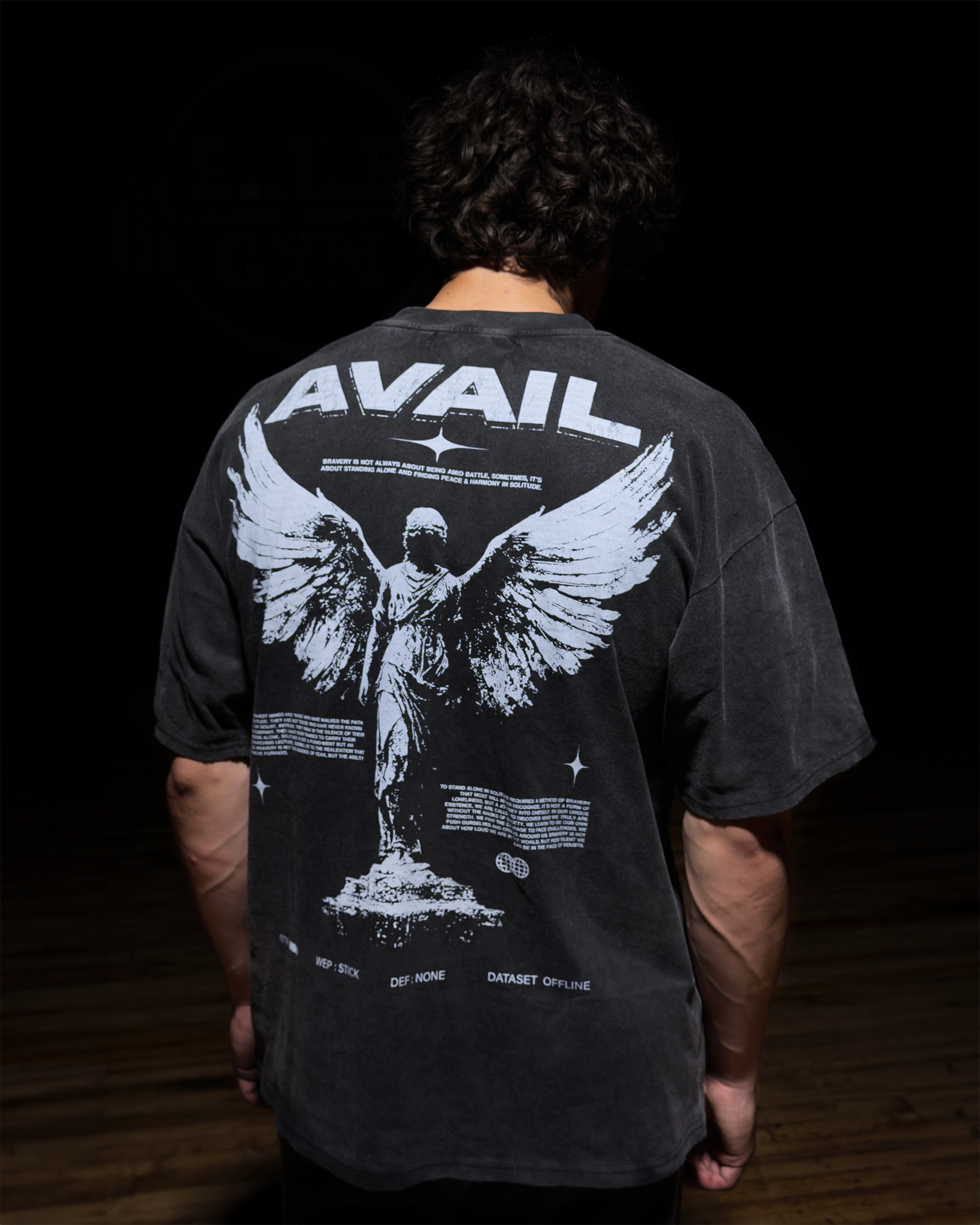 Person wearing a black t-shirt with 'AVAIL' design on the back, standing against a dark background.
