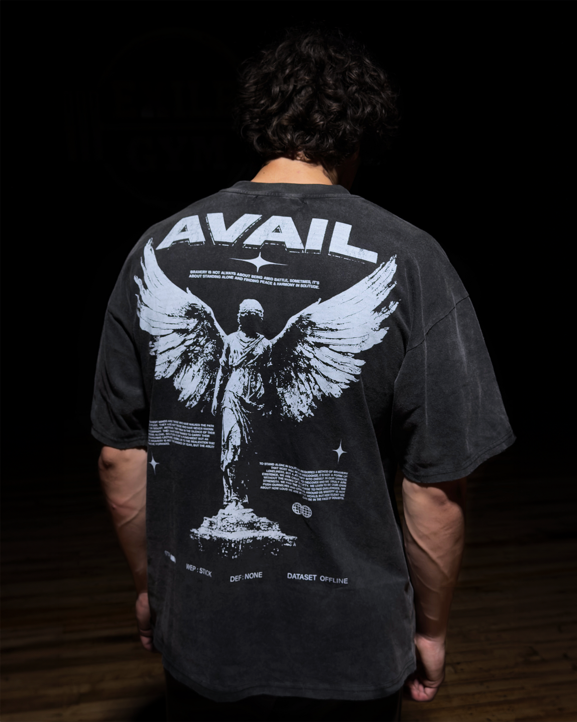 Person wearing a black t-shirt with 'AVAIL' design on the back, standing against a dark background.
